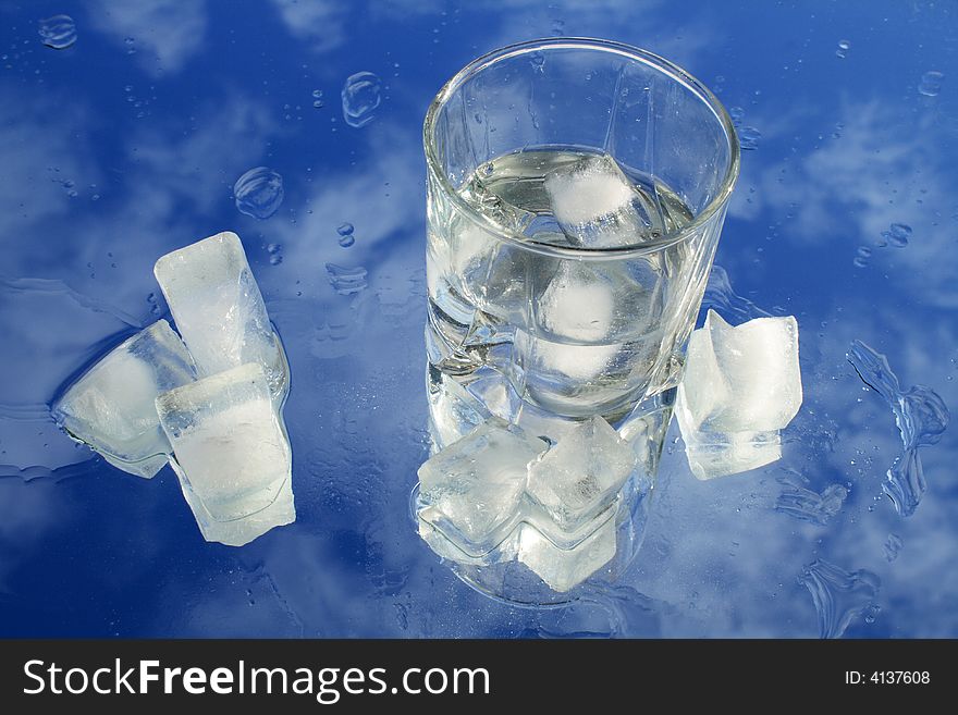 Glass of water with ice on background with blue sky and clouds. Glass of water with ice on background with blue sky and clouds