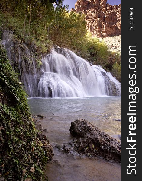 Navaho Falls cascading into aqua pool with green foliage and red rock cliff as background Havasupai Indian Reservation