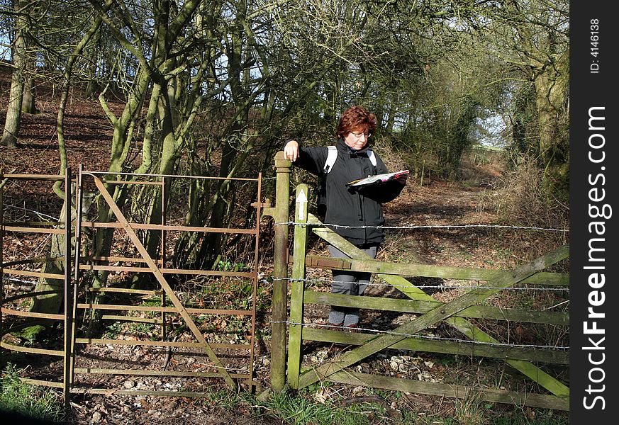 Lady Hiker Standing by a Kissing Gate reading a map on a woodland path in Rural England. Lady Hiker Standing by a Kissing Gate reading a map on a woodland path in Rural England