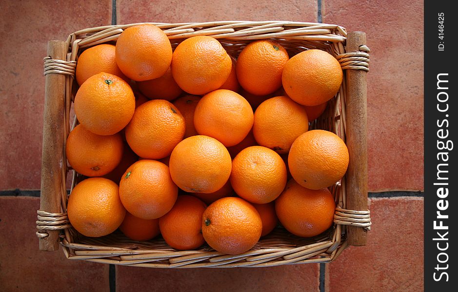 A basket of oranges on a terracotta tiled floor