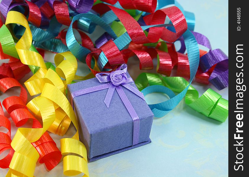 A small light purple gift box is nestled in a pile of colorful curly ribbon. A small light purple gift box is nestled in a pile of colorful curly ribbon.