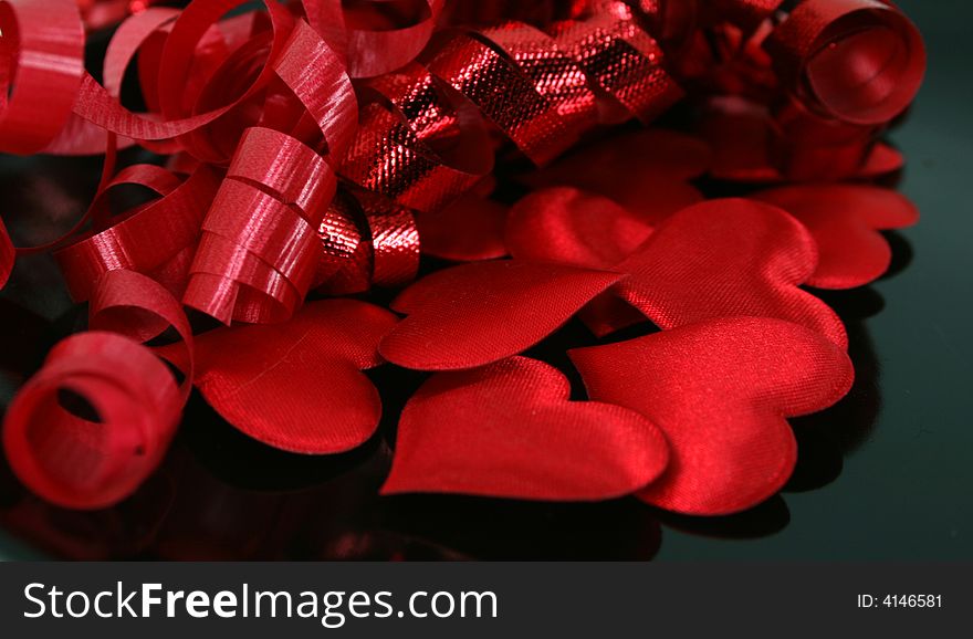 Puffy, red satin hearts with curly red ribbon on a reflective black surface. Puffy, red satin hearts with curly red ribbon on a reflective black surface.