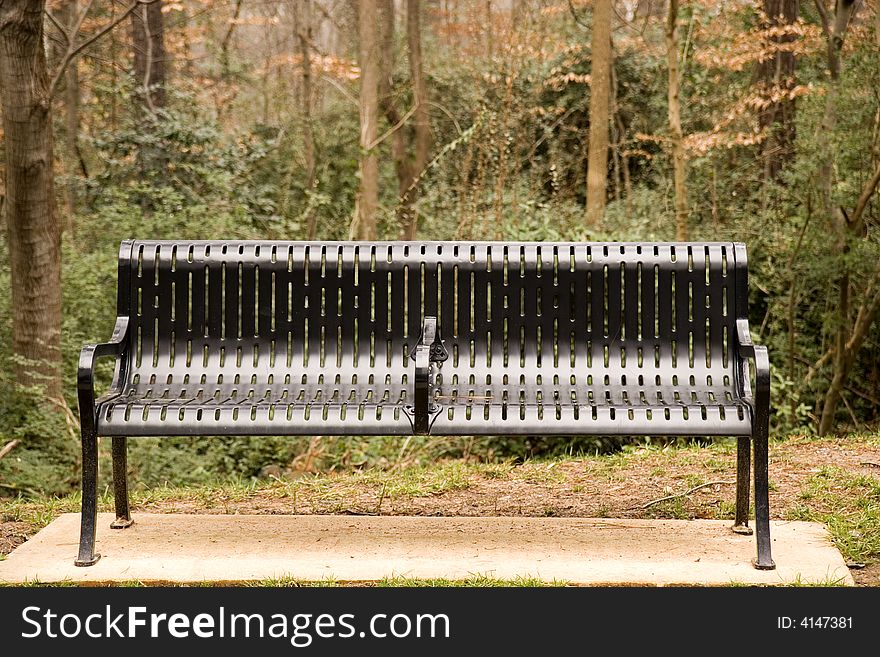 A black iron bench on a cement pad in the woods. A black iron bench on a cement pad in the woods