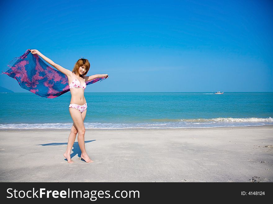A young girl in bikini holding floral scarf  walking by the beach