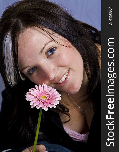 Young woman with blue eyes holding a pink flower.  Blue gel background. Young woman with blue eyes holding a pink flower.  Blue gel background