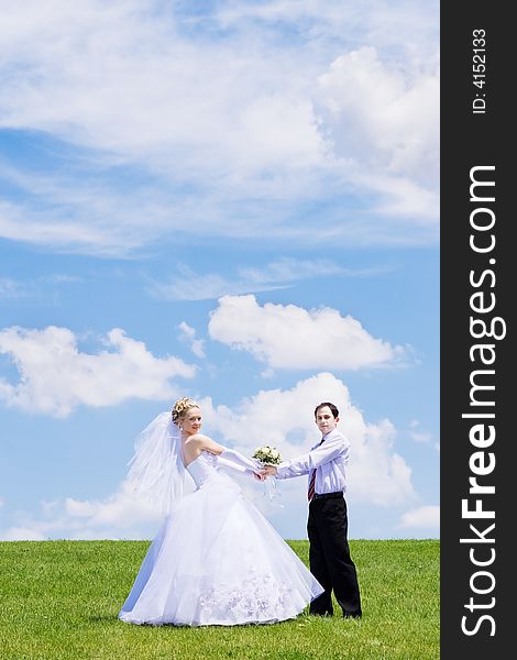 Newly-married couple on a green grass under the blue sky