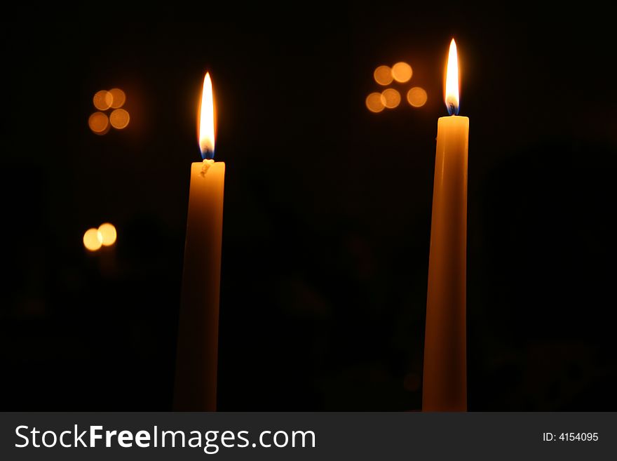Two Candles burning at night with other lights out of focus in the background