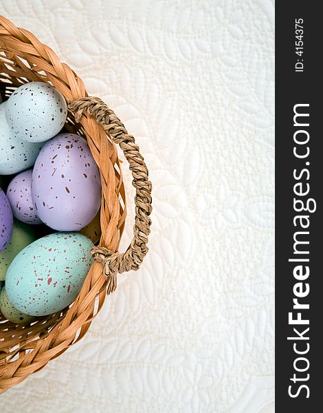 Variety of colored eggs in a basket against a quilted background.  Room for copy. Variety of colored eggs in a basket against a quilted background.  Room for copy.