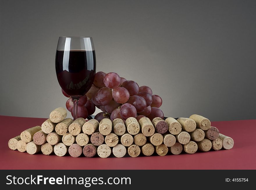 Red wine glass and grape next to group of corks over grey background. Red wine glass and grape next to group of corks over grey background.