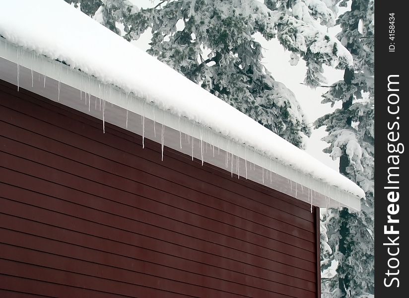 A picture of the eaves of a garage in winter with ice crystals hanging of the edge.