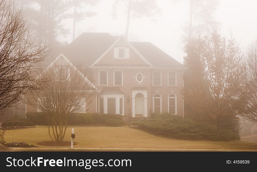 A traditional brick two story house enveloped in a dense fog. A traditional brick two story house enveloped in a dense fog