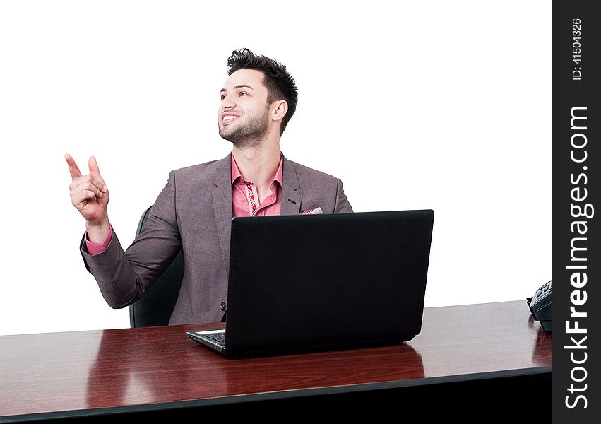 Handsome and smiling business man points with his finger in the air while sitting at his desk with a laptop. Handsome and smiling business man points with his finger in the air while sitting at his desk with a laptop