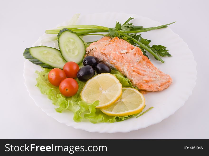 Stake from a trout with vegetables and a lemon on a plate on a white background