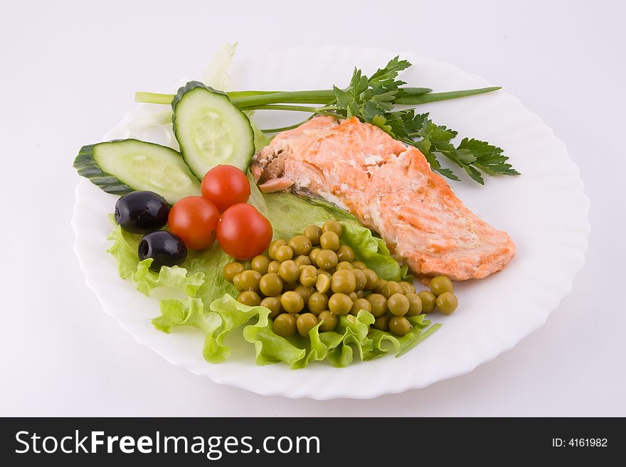 Stake from a trout with vegetables and green peas on a plate on a white background