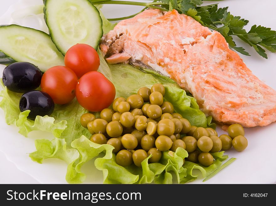 Stake from a trout with vegetables and green peas on a plate on a white background