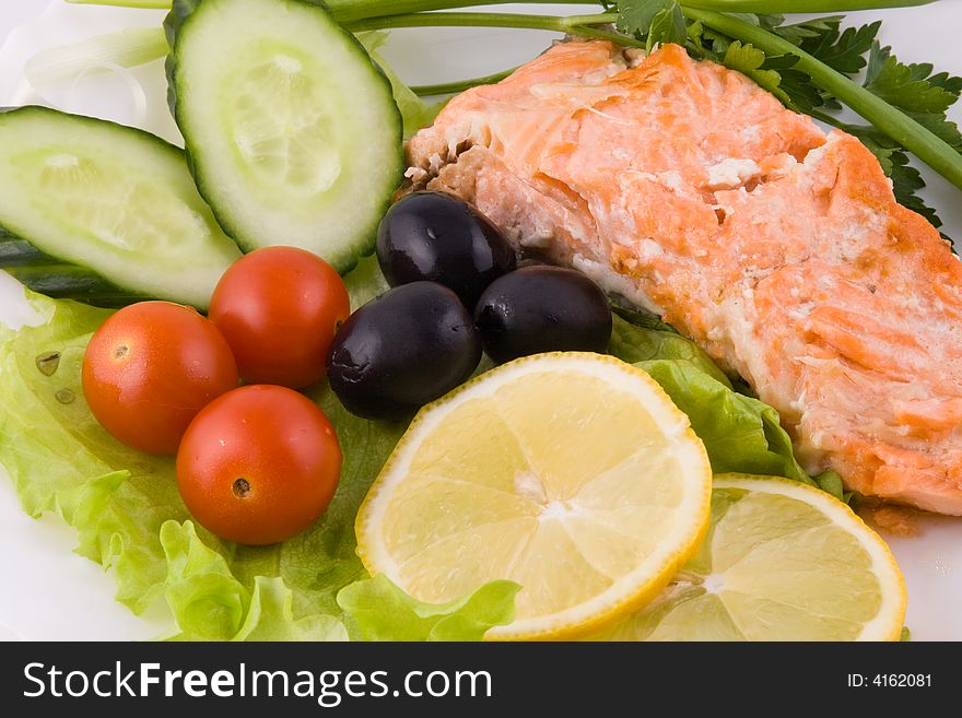 Stake from a trout with vegetables and a lemon on a plate on a white background