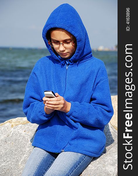 Young girl sitting on a rocks with mobile phnone at the seaside on cold and windy day. Young girl sitting on a rocks with mobile phnone at the seaside on cold and windy day.