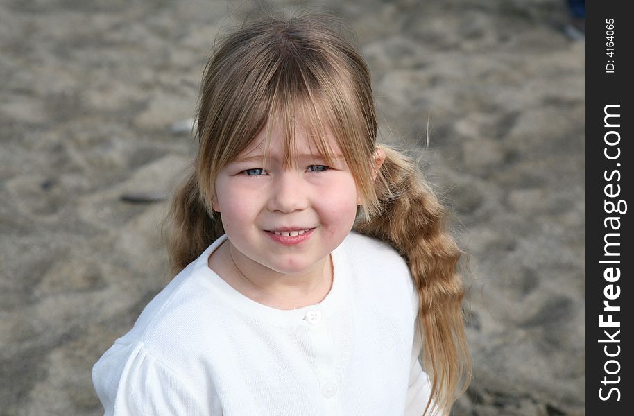 A young girl stood on the beach wearing a white jumper, looking at the camera. A young girl stood on the beach wearing a white jumper, looking at the camera