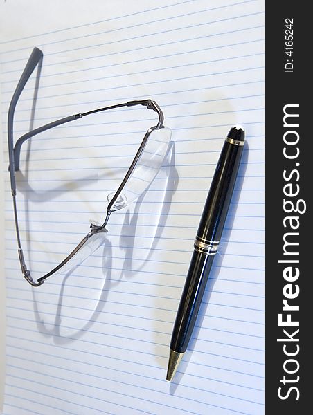 A blue lined note pad with a pen and a pair of glasses ready to take notes. A blue lined note pad with a pen and a pair of glasses ready to take notes