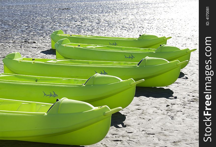 Row of green kayaks on the sand at a beach.