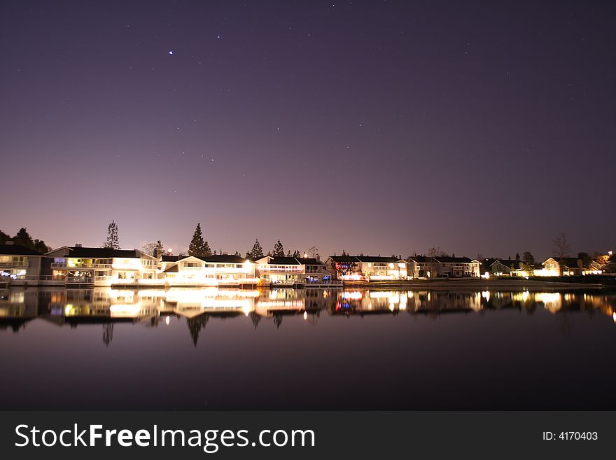 Lake side houses at night with great sky and light reflection.