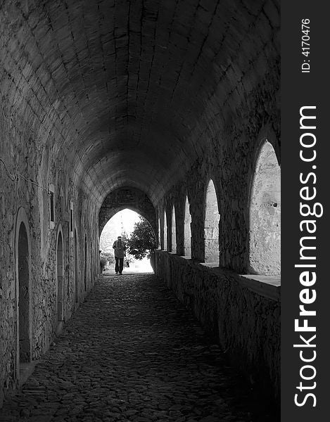 Tourist under the arches alley of the  Greek Orthodox monastery leading to the light entrance, Crete, Greece - black and white picture, noise add in purpose. Tourist under the arches alley of the  Greek Orthodox monastery leading to the light entrance, Crete, Greece - black and white picture, noise add in purpose