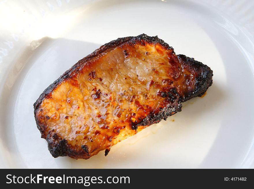 Pork loin chop grilled in th summer sunlight on a white plate. Pork loin chop grilled in th summer sunlight on a white plate