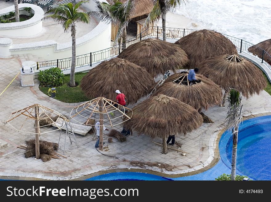 Workers building straw thatch roofed huts around a luxury swimming pool. Workers building straw thatch roofed huts around a luxury swimming pool