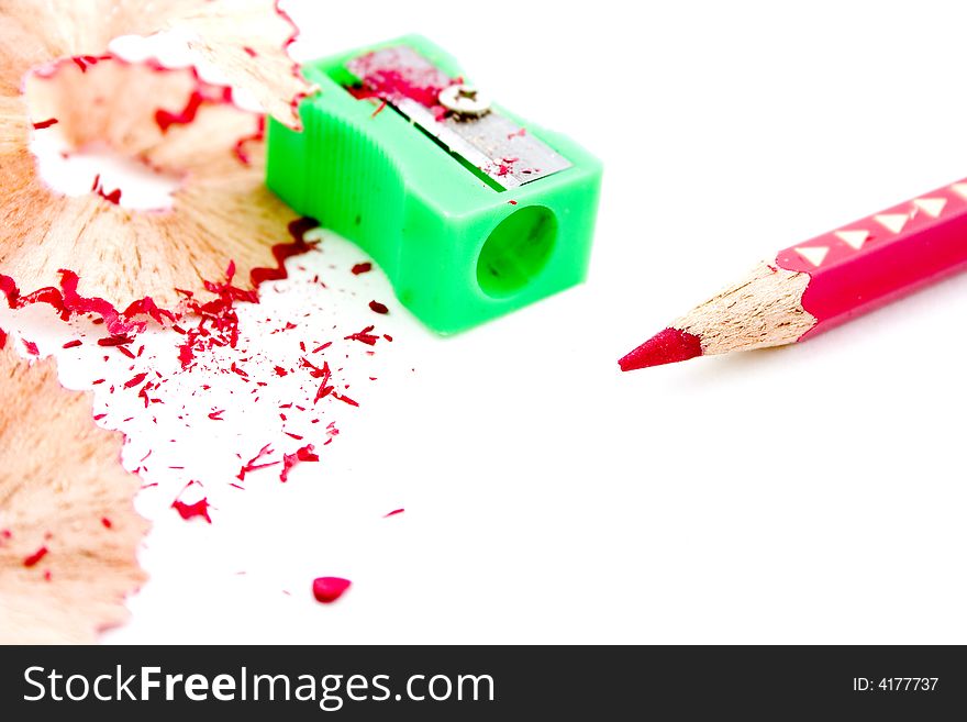 Sharpened red pencil with green sharpener in background and pencil shavings