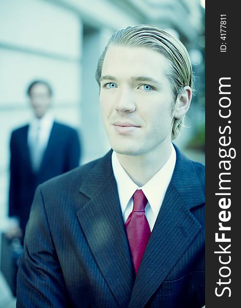 Two businessmen standing looking at camera in full suit in front of building