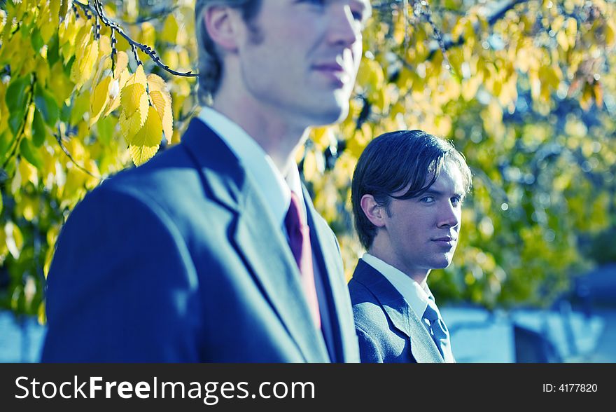 Two businessmen standing next to each other in a row under yellow leaves. Two businessmen standing next to each other in a row under yellow leaves