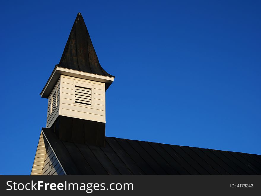 Roof and steeple of an old wooden church against a clear blue sky with space for text. Roof and steeple of an old wooden church against a clear blue sky with space for text