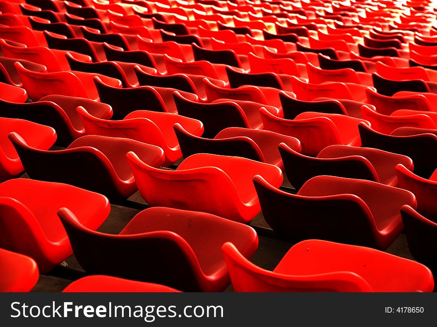 Files of red plastic seat chairs in a stadium form waves,curves and parellel lines concentrating. Files of red plastic seat chairs in a stadium form waves,curves and parellel lines concentrating.