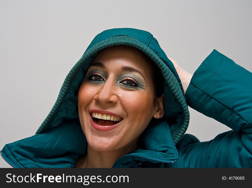 Beautiful smiling young woman wearing a green winter coat with the hood over her head and her hand behind her head, isolated on white. Beautiful smiling young woman wearing a green winter coat with the hood over her head and her hand behind her head, isolated on white