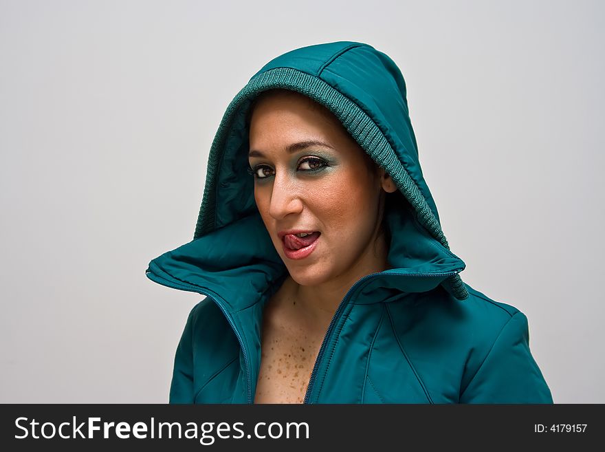 A young woman licking her lips, wearing a green winter coat zipped open and the hood covering her head, isolated on white. A young woman licking her lips, wearing a green winter coat zipped open and the hood covering her head, isolated on white