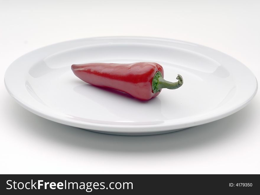 Single red chile pepper on a white plate