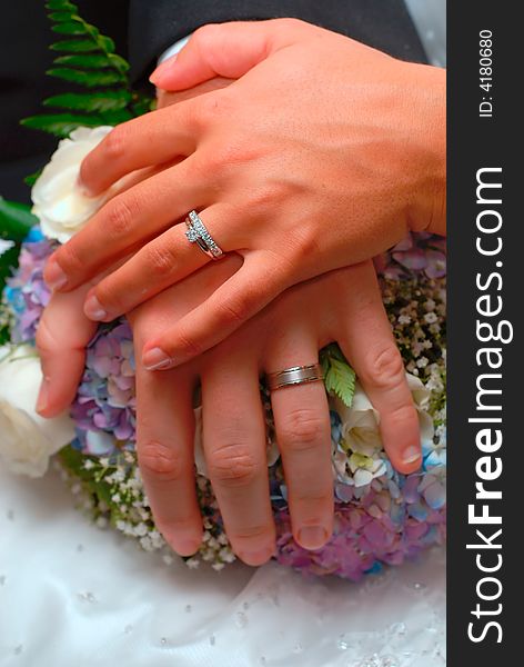 A bride and groom's hands and rings over the bride's bouquet. A bride and groom's hands and rings over the bride's bouquet.