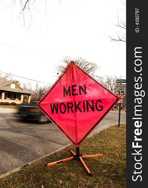 A men working sign by a busy street. A men working sign by a busy street.