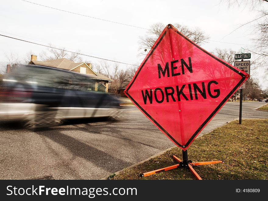 A men working sign by a busy street. A men working sign by a busy street.