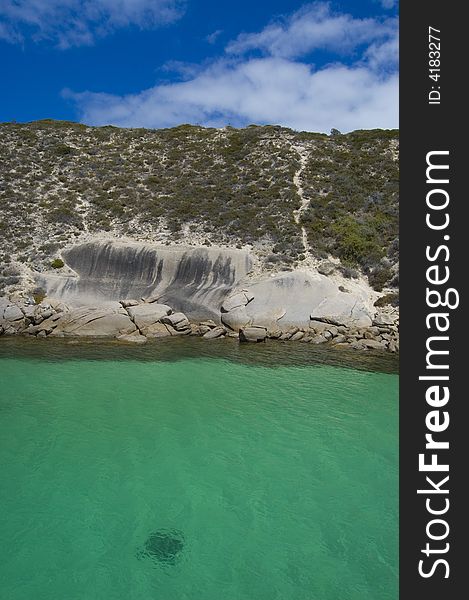 View on rocky seashore with a stingray swimming in green/turquoise water. View on rocky seashore with a stingray swimming in green/turquoise water