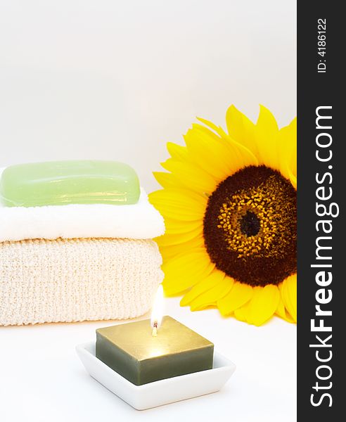 Relaxing spa scene with body sponge, face towel, glycerin soap, candle and sunflower in the background. Relaxing spa scene with body sponge, face towel, glycerin soap, candle and sunflower in the background