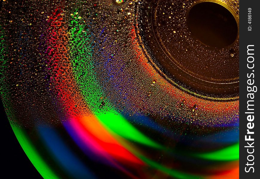 Full light spectrum on a cd quarter covered with water drops, black background. Full light spectrum on a cd quarter covered with water drops, black background