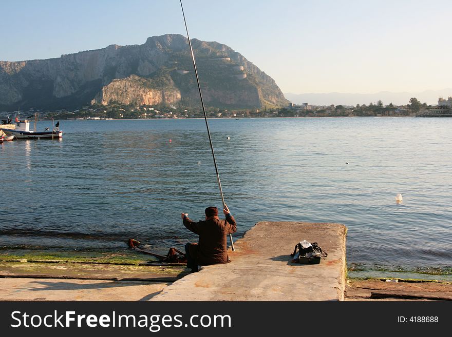 Old man fishing in the port of Mondello, near Palermo. Coast line, mont and beach. Sicily - Italy