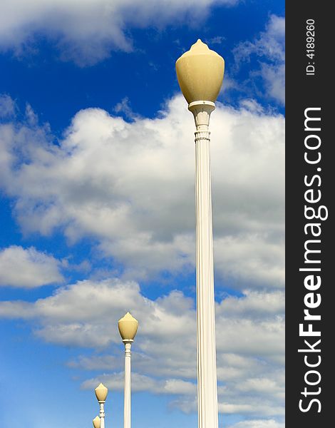 Row of lamp posts outdoors with cloudy blue sky. Row of lamp posts outdoors with cloudy blue sky