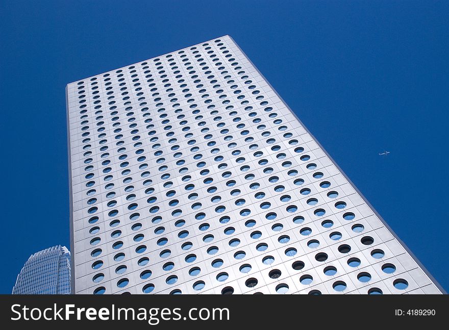 Looking up the skyscrapers in hong kong on a clear blue cloudless day a plane flys past