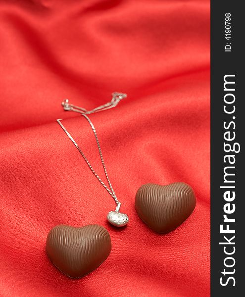 Valentines heart chocolates with silver necklace on red silk background. Valentines heart chocolates with silver necklace on red silk background
