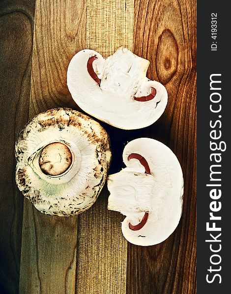 One whole and two half button mushrooms on wooden cutting board