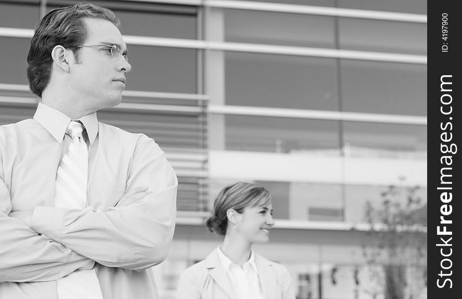 Two people standing looking to their left in front of office building, woman smiling. Two people standing looking to their left in front of office building, woman smiling