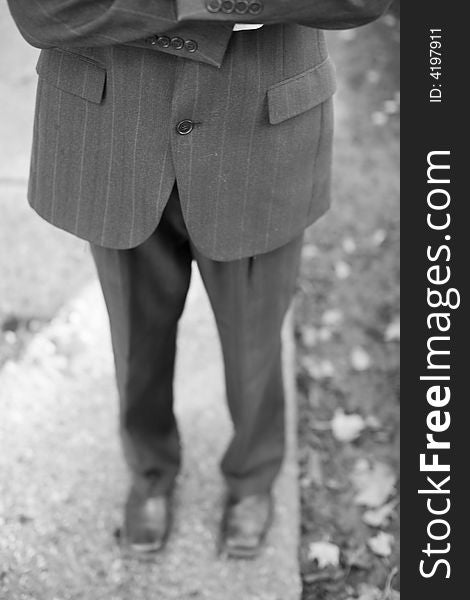 Waist-down front shot of businessman folding arms wearing suit standing on sidewalk. Waist-down front shot of businessman folding arms wearing suit standing on sidewalk