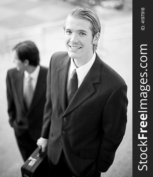 Two businessmen standing on steps in suits holding briefcase looking up while other is looking away